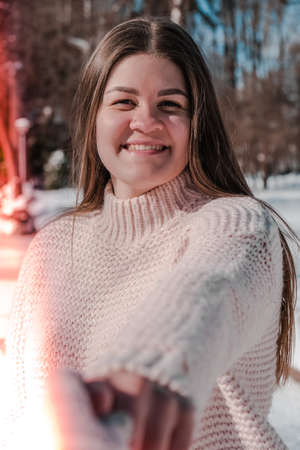 Beautiful young woman in knitted sweater in winter park. Cold weather outdoors. Snow Happy smiling portrait of girl. Winter fashionの写真素材