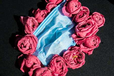 New normal mock up, pink roses or peonies with blue medical protective face mask. Creative minimalistic style. Trend. Quarantine self isolationの写真素材
