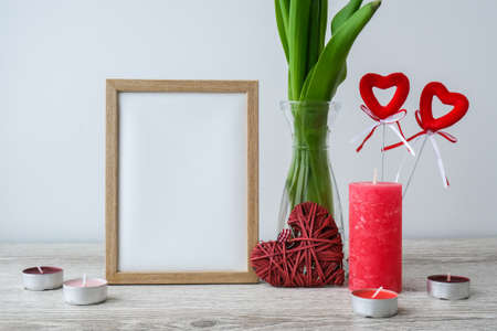 Holiday mock up. Tulip flowers in glass vase with picture frame decor on wooden table background...