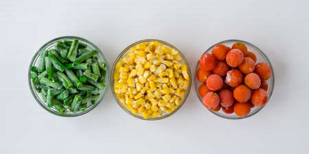 Three Bowls of frozen vegetables food of yellow corn, green beans, red tomatoes. Colors of traffic...