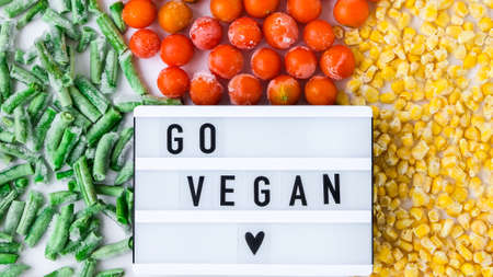 Lightbox with text GO VEGAN frozen vegetables food of yellow corn, green beans, red tomatoes. Colors of traffic light. Harvest Food preservation for winter. Copy spaceの写真素材