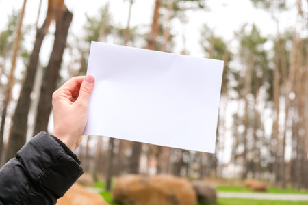 Female hands standing with white empty paper sheet outdoors. Nature background.の写真素材