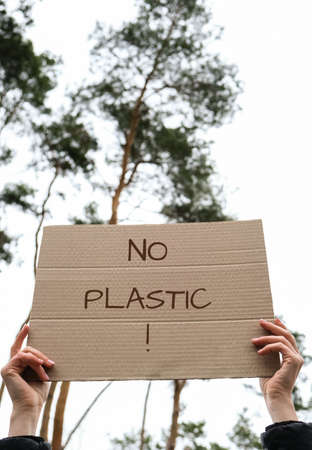 Female hands holding cardboard with text NO PLASTIC outdoors. Nature background. Protester activistの写真素材