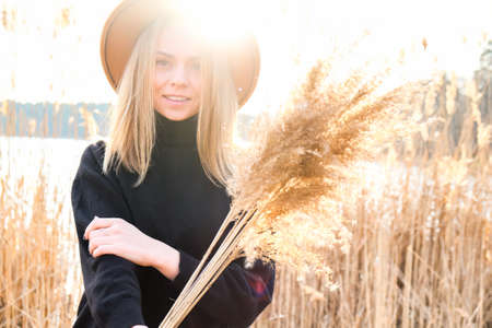 European blonde woman with beige hat in black sweater in the countryside. Golden hour, cottagecore. Local travel. Slow living. Mental health. Earth tones. Pampas grassの写真素材