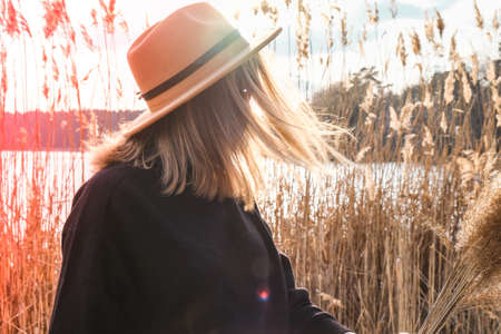 European blonde woman with beige hat in black sweater in the countryside. Golden hour, cottagecore. Local travel. Slow living. Mental health. Earth tones. Pampas grassの写真素材