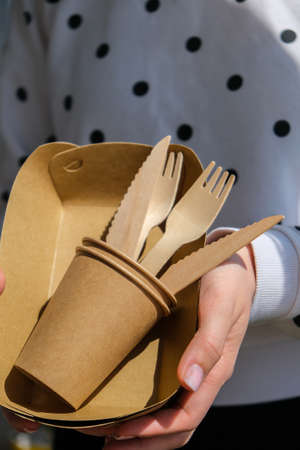 Female hands holding Wooden forks and paper cups with plates. Eco friendly disposable tableware....