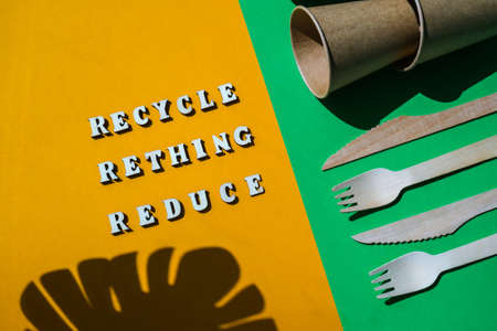 RECYCLE RETHING REDUCE text Wooden forks and paper cups with plates on color background. Eco...