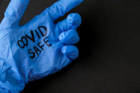 Blown up blue latex surgical glove on black background. Reopening covid safe. Open again text...