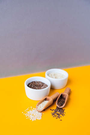 Wooden spoons with sesame and flax seeds lies in a white mortar on a yellow background. Healthy...