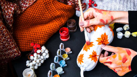 DIY. Do it yourself. Woman paints thanksgiving decorations on orange pumpkin for Halloween. Autumn...