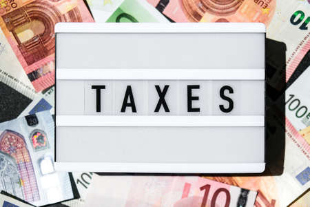 Lightbox board with word TAXES in black letters around Euro banknotes. Tax payment and filing concept. Money, Business, finance, investment, saving and corruptionの写真素材