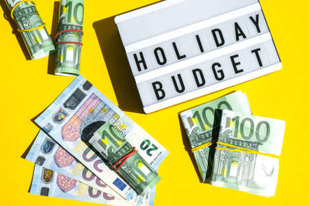 Lightbox board with word HOLIDAY BUDGET on yellow background around euro banknotes. Money, Business, finance, investment, savingの写真素材