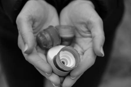 Black and white Closeup at caucasian female hands full of plastic bottle cups, handful of waste of plastic lids. Recycling. Collecting bottle caps. Environment conceptの写真素材