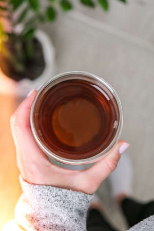 Top view of female hand holding cup of black tea. Breakfast morning concept. Green plant on...