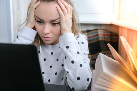 Young woman sitting on balcony next to laptop bored, stress upset. Online education. Stay home concept. Work from home. Earphonesの写真素材