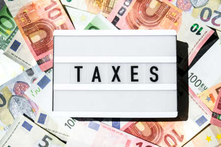 Lightbox board with word TAXES in black letters around Euro banknotes. Tax payment and filing concept. Money, Business, finance, investment, saving and corruption. Cash billの写真素材