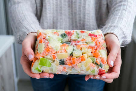 Mixed vegetable frozen food briquette in female hands. Preparing harvest for winter. Veganism, vegetarian healthy eatingの写真素材