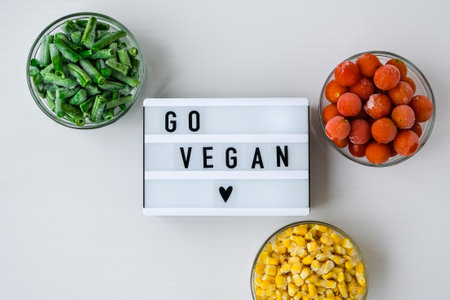 Lightbox with text GO VEGAN Three Bowls of frozen vegetables food of yellow corn, green beans, red tomatoes. Colors of traffic light. Harvest Food preservation for winter.の写真素材
