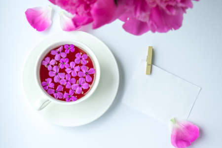 Creative layout with pink peonies flowers and cup of tea on bright table. Paper note. Copy space. Spring Seasonal valentine, woman, mother, 8 march holiday, romance breakfast. Stylish blogger. Greeting card. Invitation. Blog postの写真素材