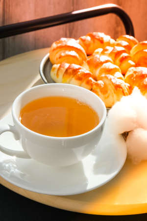 Traditional French croissants in a plate, cup of tea in background. Cotton branch. Selective focus....