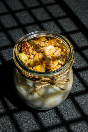 Healthy breakfast. Oatmeal Granola with greek yogurt and nuts banana muesli in jars on dark...
