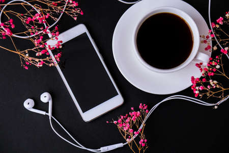Headphones mobile phone. Black screen. Copy space for text. Top view. Dry pink flowers decoration. Workplace. Black coffeeの写真素材