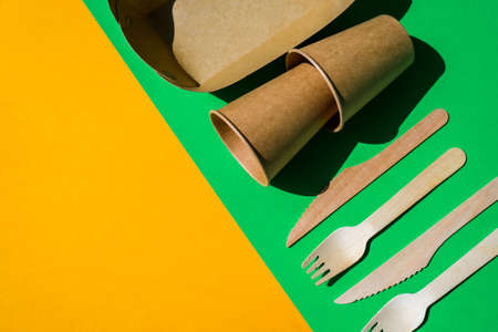 Wooden forks and paper cups with plates on color background. Eco friendly disposable tableware. Used in fast food, restaurants, takeaways, picnics. No plasticの写真素材