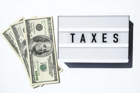 Lightbox board with word TAXES in black letters around Us dollars banknotes. Tax payment and filing concept. Money, Business, finance, investment, saving and corruption. Cash billの写真素材