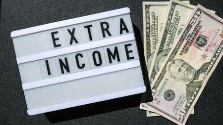 Lightbox board with word EXTRA INCOME in black letters around US dollar banknotes. Money, Business, finance, investment, saving. Cash bill. Business budget of wealth and prosperity finance. Passive incomeの写真素材