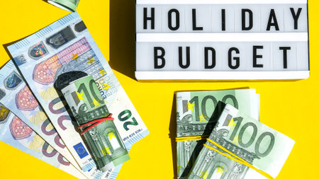 Lightbox board with word HOLIDAY BUDGET on yellow background around euro banknotes. Money, Business, finance, investment, saving. Cash bill. Business budget of wealth and prosperity finance. Passive incomeの写真素材