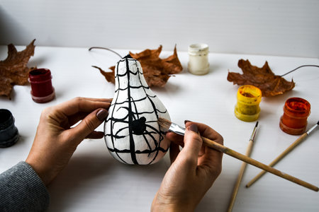 Woman paints spider on pumpkin for Halloween. Autumn leaves. Diy children craft. Do it yourself. Autumn party decorationsの写真素材