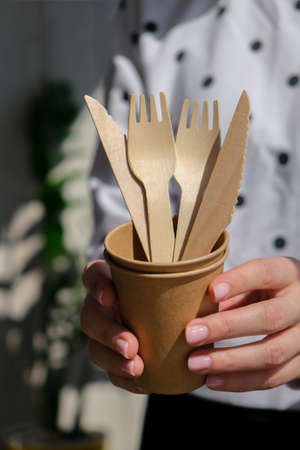 Female hands holding Wooden forks and paper cups with plates. Eco friendly disposable tableware....