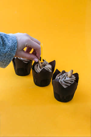 Female hands making Delicious chocolate cupcakes with cream on yellow background. Three chocolate...