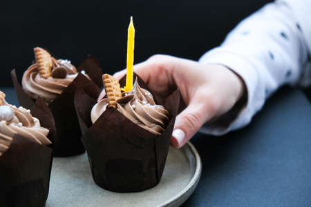 Female hands making Delicious chocolate cupcakes with cream on dark background. Three chocolate muffin. Birthday cake party preparation. Homemade Chocolate Cupcakeの写真素材