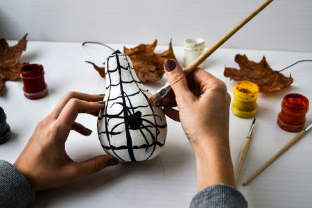 Woman paints spider on pumpkin for Halloween. Autumn leaves. Diy children craft. Do it yourself. Autumn party decorationsの写真素材
