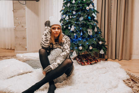 Beautiful young girl sitting next to the christmas tree. New year decoration. Home interior. Winter holidaysの写真素材
