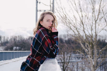 Curly blond pretty young woman in poncho in winter park. Cold weather. Holidays, season and leisure concept. Christmas, New year. Winter fashion, holidays, rest, travel concept.の写真素材