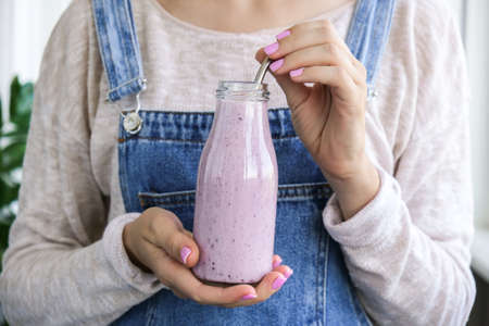 Female hands holding Blueberry smoothie topped with blueberries. Woman eating glass of breakfast protein smoothie drink made from pureed raw blueberries, banana, milk, yogurt, and cottage cheese. Vegetarian vegan foodの写真素材