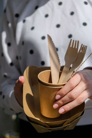 Female hands holding Wooden forks and paper cups with plates. Eco friendly disposable tableware. Used in fast food, restaurants, takeaways, picnics. No plastic zero wasteの写真素材