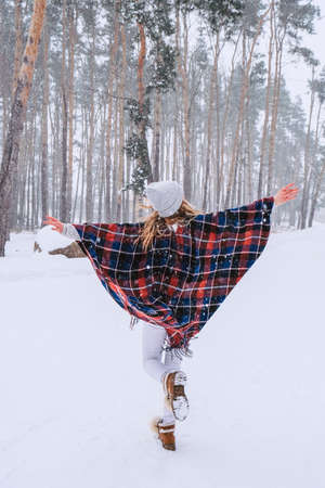 Dancing woman traveling among forest wearing hat and poncho, boho and wanderlust style. Winter is...