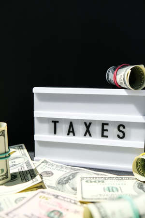 Lightbox board with word TAXES in black letters around Us dollars banknotes. Tax payment and filing concept. Money, Business, finance, investment, saving and corruption. Cash billの写真素材