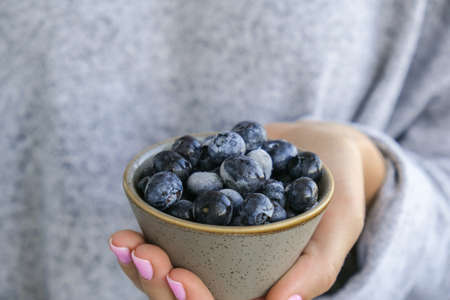 Woman holding bowl with Frozen blueberry fruits. Harvesting concept. Female hands collecting...