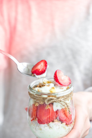 Female hands woman eating Healthy breakfast. Oatmeal Granola with greek yogurt and nuts strawberry muesli in jars on light background. Fitness. Weight loss diet concept. Detox menu. Healthy eating foodの写真素材