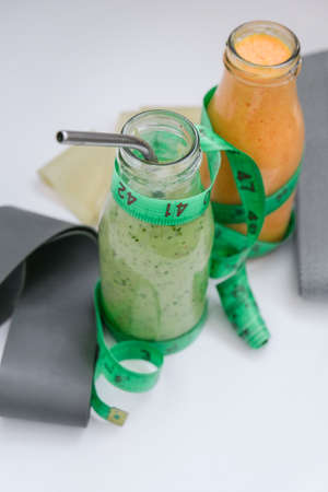 Seasonal Matcha green vegan smoothie and pumpkin carrot smoothie drink detox Breakfast with measuring tape and rubber resistance band. Stretch fitness band. Clean eating, weight loss, healthy dieting food concept. Staying healthy at homeの写真素材