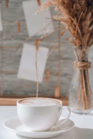 White home office room interior, bloggers workplace. Cup of coffee. Mood board with postcards and reminders mockup. Cotton branches in a vase, interior decoration. Feminine hipster office table decoration. Freelance workplaceの写真素材