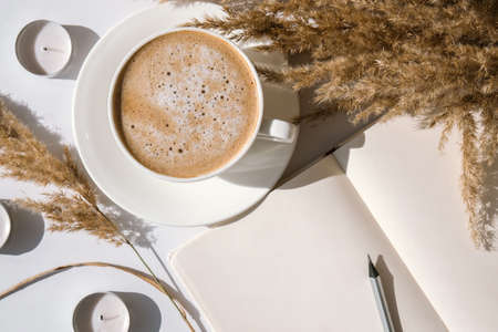 Pampas grass and white cup with coffee. Empty notebook making a plan for the day. Drinking Cappuccino in the breakfast morning at home. Flat lay. Wallpaper. Aesthetics cozy homeの写真素材