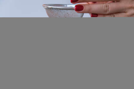 Adding cacao powder on top of hot chocolate with marshmallows in white cup on sweater background. Cozy christmas lights. Preparation for new year holidays atmosphereの写真素材