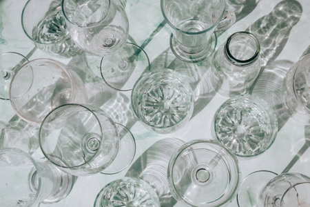 Beautiful different glasses stand on white background in sunlight and create shadows. Hard light,...
