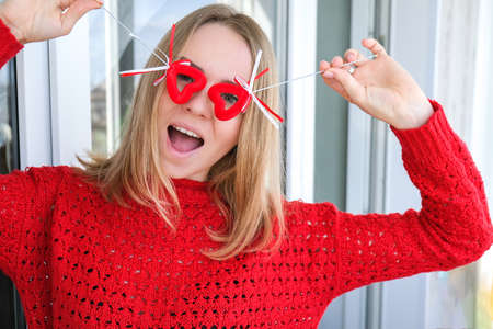 Young blonde girl in red sweater holding red hearts showing emotions. Taking selfie. Video chat. Love in distance. Stay home. Valentines day. Romantic aloneの写真素材