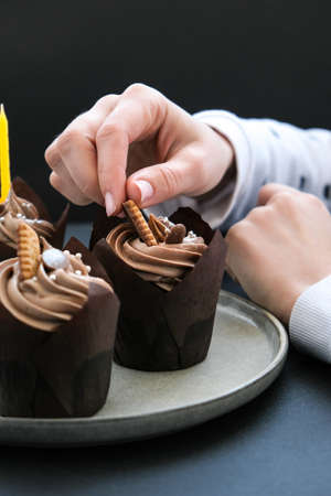 Female hands making Delicious chocolate cupcakes with cream on dark background. Three chocolate muffin. Birthday cake party preparation. Homemade Chocolate Cupcakeの写真素材